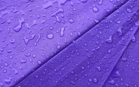 Gotas de chuva em close sobre tecido de guarda-chuva roxo, textura macro