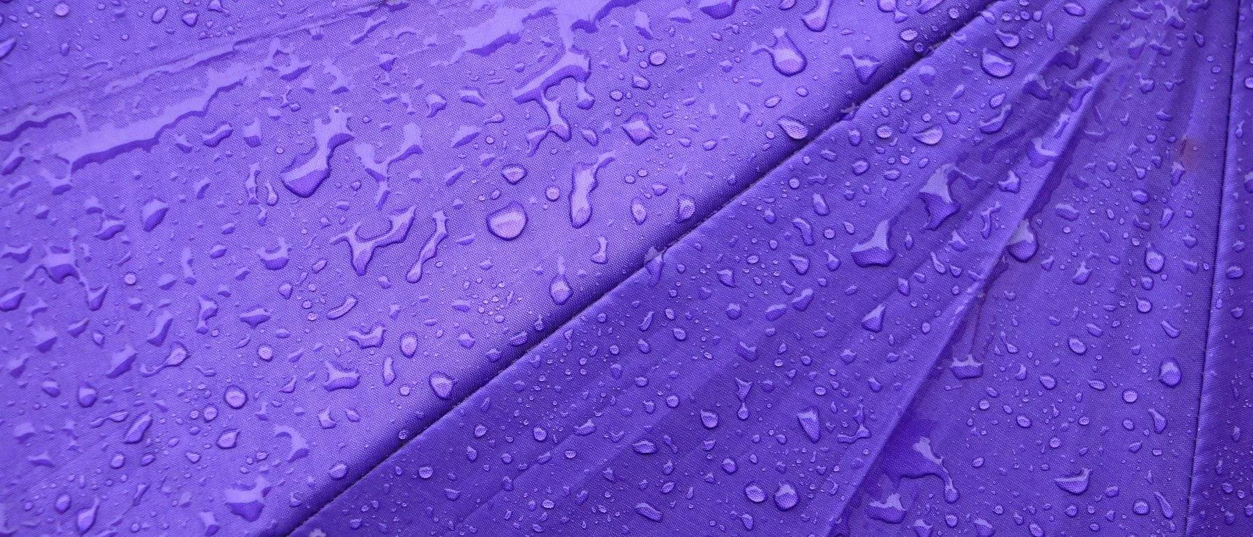 Gotas de chuva em close sobre tecido de guarda-chuva roxo, textura macro