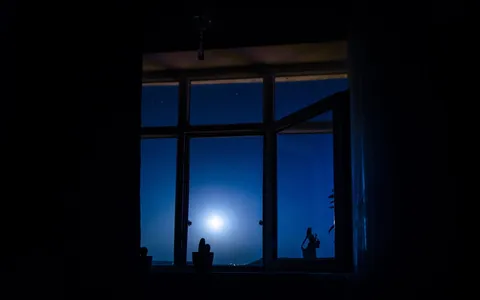 Janela escura de quarto à noite com a lua cheia ao fundo, silêncio e insônia
