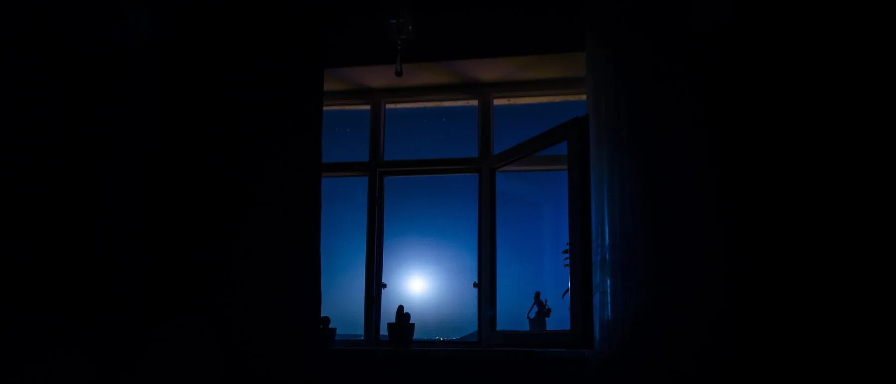 Janela escura de quarto à noite com a lua cheia ao fundo, silêncio e insônia