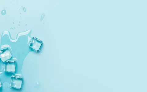 Cubos de gelo derretendo sobre superfície azul clara, sensação de frio