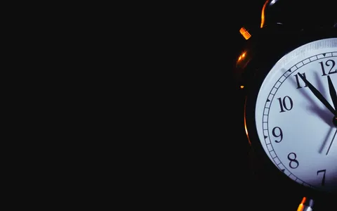 Despertador antigo marcando quase meia-noite, com luz quente e fundo escuro